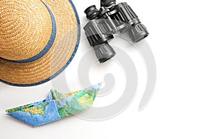 Straw hat, binoculars and a paper boat folded from a map on a white background, concept for cruise or vacation on the sea, copy