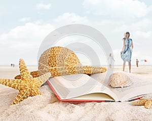 Straw hat , book and seashells in the sand