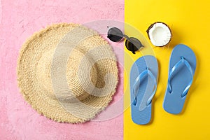 Straw hat, flip flops, sunglasses and coconut on two tone background, space for text and top view. Summer vacation