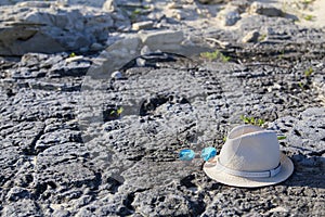 A straw hat and glasses lie on a rock on the beach.