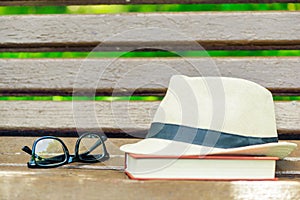 straw hat, glasses and a thick book on a wooden bench