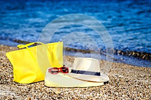 Straw hat, glasses, yellow beach bag and beach towel on the sand on the beach.