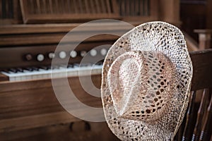 Straw hat hanging on a chair post next to an organ.