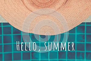 Straw hat at the pool edge with Hello summer wording