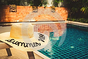 Straw hat at the pool edge with palm reflections in the water. Private pool in the asian style garden