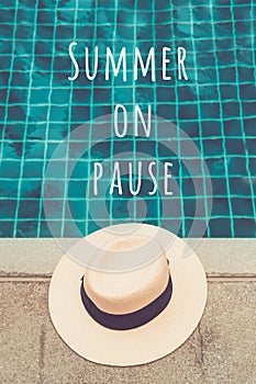 Straw hat at the pool edge with Summer on pause wording