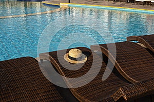 Straw hat on rattan brown sun loungers near the swimming pool. Relaxation and loneliness concept