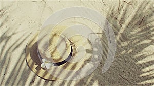 Straw hat on sand, sun protection concept. Still life with a hat and shades of palm leaves.