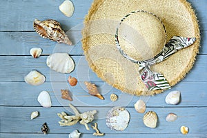 Straw hat and seashells on a light blue wooden plank background. Top view flat.