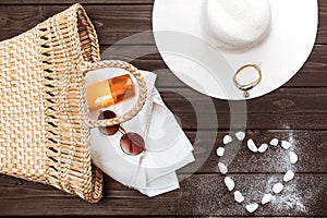 Straw hat, sun cream, towel and sunglasses in bag, heart made of stones on table