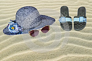 Straw hat, sun glasses and flip flops on sandy beach. Backdrop for summer holidays and travel advertising with space. Beach