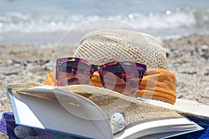 Straw hat sunglasses and a book on the beach