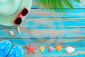 Straw hat, sunglasses, slipper, starfish and shellsn on wood plank in blue sea paint color background.