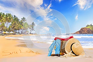 Straw hat, sunglasses, slippers and a bag on the golden sand of Sri Lanka`s beach