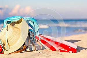 Straw hat, umbrella and blue bikini bra swimsuit with beach bag against the ocean beach with beautiful blue sky and clouds.