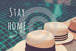 Straw hats at the pool edge with palm reflections in the water with Stay home wording