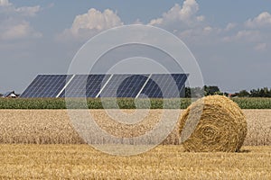 Straw roll bales with crop field, photovoltaic panel and blue sky in background