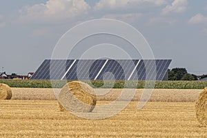 Straw roll bales with crop field, photovoltaic panel and blue sky in background