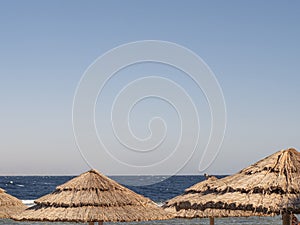 Straw Roof Of Beach Umbrella And Blue Sky With Ocean In Background. Beach Vacation And Travel Concept