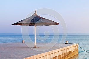 Straw umbrella on tropical idyllic resort. Blue sea and sky with soft yellow sunlight on sunset. Happy vacations concept