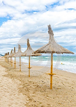 Straw umbrellas on beautifull beach in a windy day with fine san