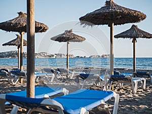 Straw umbrellas and blue sunbeds in a mediterranean beach
