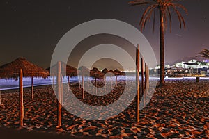 Straw umbrellas on empty beach in Marbella, Spain. Night photography with stars