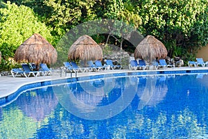 Straw umbrellas and lounge chairs around outdoor swimming pool. Riviera Maya, Cancun, Mexico