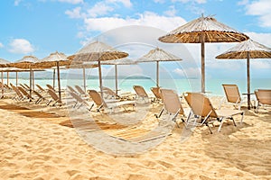 Straw umbrellas and sunbeds on a sunny golden tropical beach seashore