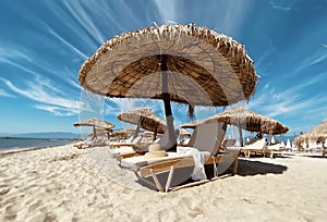 Straw umbrellas and wooden sun loungers wooden table on the bed blue sky, sea, white sand on the beach summer resort in Greece sum