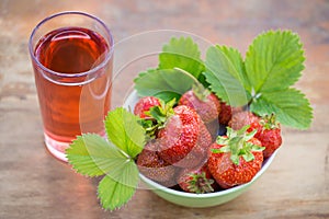 Strawberries in a bowl and a glass of strawberry juice on a wooden table