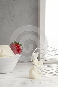 Strawberries in bowl with whipped cream and wire whisk