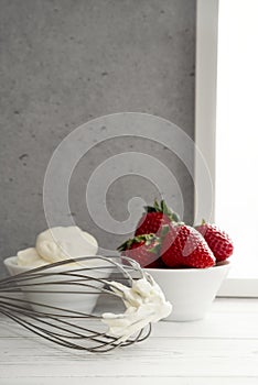 Strawberries in bowl with whipped cream and wire whisk