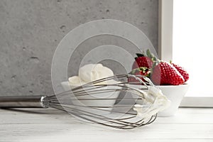 Strawberries in bowl with whipped cream and wire whisk