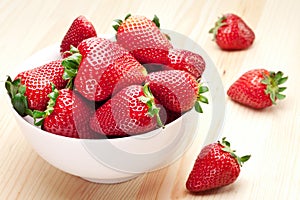 Strawberries in the bowl on wooden table.