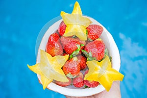 Strawberries and carambola are laid out in a half of coconut, on a blue background.