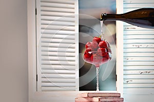 Strawberries and champagne. Berry in tall glass. Champagne pours on strawberries. Photo on the background of the window.