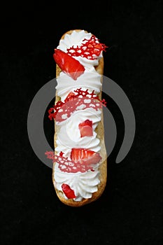 Strawberries and cream eclair with fresh berries and red lace tuile top down on black background