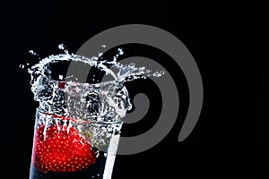 Strawberries fall into a glass of water. Water spills out of a glass.