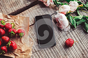 Strawberries, flowers and phone on the rustic table. Healthy breakfast, Clean eating, vegan food concept.