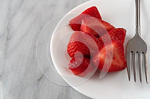 Strawberries and a fork on a white plate atop a marble counter top