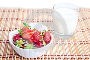 Strawberries and glass of milk on straw mat