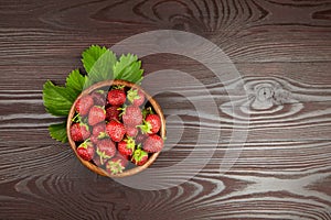 Strawberries with green leaves in wooden bowl on table, top view. Red ripe berries, fresh juicy strawberry on wooden background