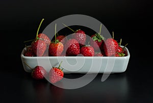Strawberries are housed in white ceramic vessels on a black background.