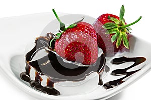 Strawberries on an ice cream drizzled by chocolate on a white p