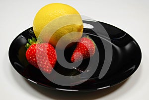 Strawberries and lemon in a black plate