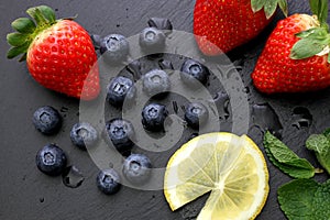 Strawberries, lemon slices, mint leaves and blueberries on black slate background