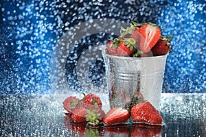 Strawberries in a metal bucket closeup under the water drops in a dark blue background. Healthy lifestyle. Multivitamin cocktail.