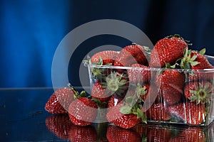 Strawberries in a plastic box closeup under the water drops in a dark blue background. Healthy lifestyle. Multivitamin cocktail.