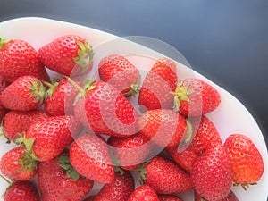 Strawberries on a plate, black background. White dishes and delicious red large garden strawberries. Healthy food